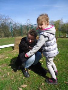 Frau und Mädchen streicheln kleinen schwarzen Hund auf einer Wiese im Tierheim Siegen.