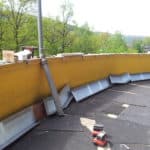 Gelbe Dachbrüstung mit verstreuten Werkzeugen und Metallabdeckungen.