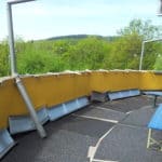 Geschwungene gelbe Wand, blaue Bänke und Bäume im Tierheim Siegen.