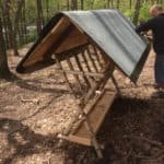 Eine Person baut einen Holzunterstand mit Schrägdach im Wald beim Tierheim Siegen.