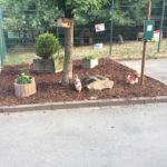 Garten am Weg mit Pflanzgefäßen, Hühnerstatuen und Baum.