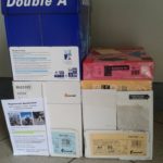 Vier Kisten mit A4-Papierstapeln auf einem gefliesten Boden.