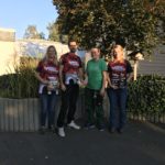 Vier Personen vor dem Tierheim Siegen, in der Nähe von Pflanzen; drei in passenden Hemden, eine Frau in Grün.