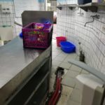 Küche mit freiliegenden Bodenrohren, Reinigungsmitteln und Körben.