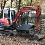 Roter Kubota-Bagger hebt Kiste in der Nähe des Zauns im Laubwald an.