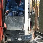 Mann in blauer Jacke benutzt Kubota-Bagger in der Nähe von Bäumen im Tierheim Siegen.