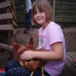 Kind in rosa Hemd im Freien, hält ein braunes Huhn.