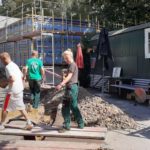 Drei Bauarbeiter tragen Material auf einer Baustelle.