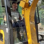 Ein Mann lächelt im Inneren eines gelben JCB-Baggers im Tierheim Siegen.