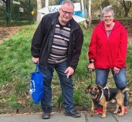 Zwei lächelnde Erwachsene mit einem glücklichen Hund an der Leine im Tierheim Siegen.