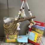 Weißer Nymphensittich auf Seilbarsch mit Vogelfuttertüten und blauem Zettel.