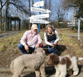 Zwei Menschen mit zwei Hunden bei einem Wegweiser im Tierheim Siegen.