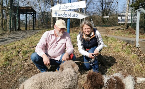 Zwei Menschen mit zwei Hunden bei einem Wegweiser im Tierheim Siegen.