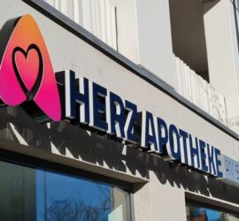 HERZAPOTHEKE-Schild mit Herz-Logo an der Außenseite des Gebäudes.