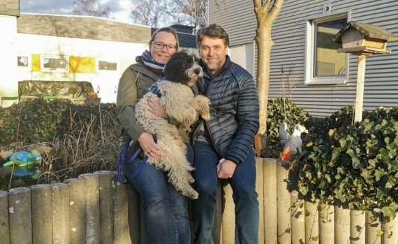 Zwei Menschen im Freien lächeln und halten einen schwarz-weißen Hund.