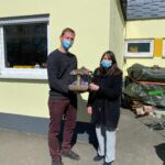 Zwei Maskierte halten eine braune Tasche vor dem Tierheim Siegen.