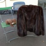 Brauner Pelzmantel und Plüschtier auf grünen Stühlen im Freien.