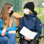 Zwei vermummte Personen unterhalten sich auf einer Bank vor dem Tierheim Siegen; eine hält ein Heft in der Hand.
