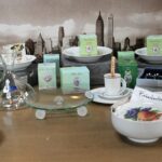 Küchengeschirr, Gläser und Teedosen auf einem Tisch; dahinter Stadtansicht.