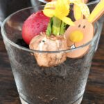 Glas mit Erde, gelber Zwiebel, rotem Ei und Papierhäschen.