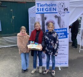 Drei lächelnde Mädchen mit einem Geschenkkorb in der Nähe des Tierheims Siegen-Banner.