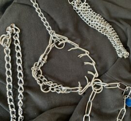 Vier Hundehalsbänder aus Metall mit einzigartigen Ketten auf schwarzem Stoff.