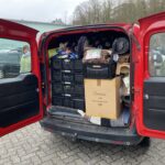 Ein roter Lieferwagen mit offenen Hintertüren, vollgepackt mit Kisten; Person in der Nähe.