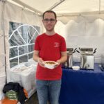 Ein Mann im roten Hemd hält eine Schüssel mit Lebensmitteln in einem Zelt in der Nähe von Buffet-Tabletts.