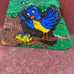 Gemalter Felsen eines blauen Vogels, der drei gelbe Küken im Nest füttert.