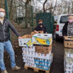Drei Maskierte stehen neben Konservendosen und Kartons in der Nähe eines Transporters vor dem Tierheim Siegen.