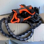 Hundegeschirr und geflochtene Leine auf offenem Karton an einer weißen Wand.