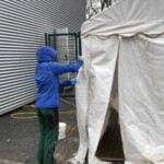 Person in blauer Jacke reinigt weißes Zelt im Tierheim Siegen.