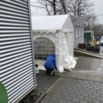 Person in blauer Jacke hockt an einem regnerischen Tag vor einem weißen Zelt.