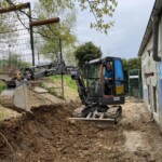 Eine Person gräbt mit einem Bagger in der Nähe eines Gebäudes im Tierheim Siegen.