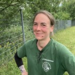 Lächelnde Frau in grünem Hemd mit Kratzern im Gesicht am Zaun, im Freien.