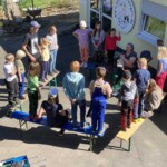 Kinder und Erwachsene auf Bänken vor dem Tierheim Siegen in der Sonne.